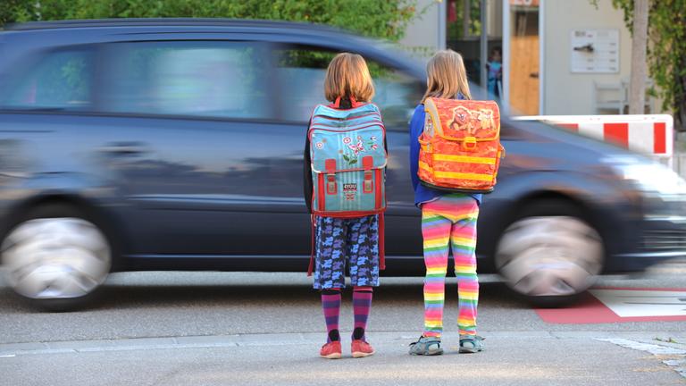 Schülerinnen stehen in Freiburg an der Strasse vor einem vorbeifahrenden Auto.