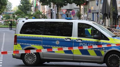 Ein Fahrzeug der Polizei steht hinter einer Absperrung auf einer Straße nachdem Schüsse am 31.08.2026 auf ein Café in Köln abgefeuert wurden.