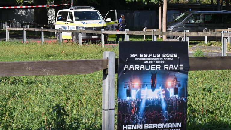 Polizisten sichern am 30.08.2026 in Aarau, in der Nordschweiz, den Bereich hinter einem Plakat ab, auf dem für eine Rave-Party geworben wird, bei der es zu einer Schießerei gekommen war.