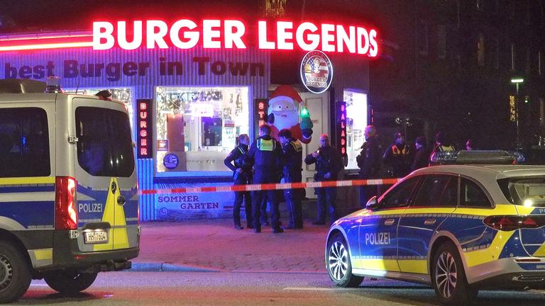 Einsatzkräfte der Polizei stehen vor dem Tatort, einem Burgerladen im Hamburger Bezirk Eimsbüttel, aufgenommen am 02.12.2025