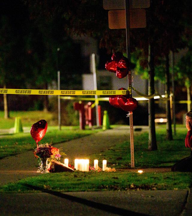 Vor dem Tatort an einer Grundschule in Oregon wurden in gedenken an die Opfer Luftballons und Kerzen aufgestellt. Eine Person kniet vor der Gedänkstätte.