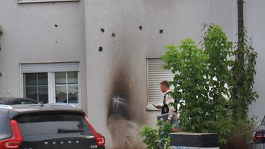 Auf dem Bild zu sehen: Die Fassade eines Wohnhauses in Lampertheim weist mehrere Einschusslöcher auf. In der Mitte der Hauswand sind deutliche Rußspuren zu sehen, die auf einen Brandkörper hindeuten.