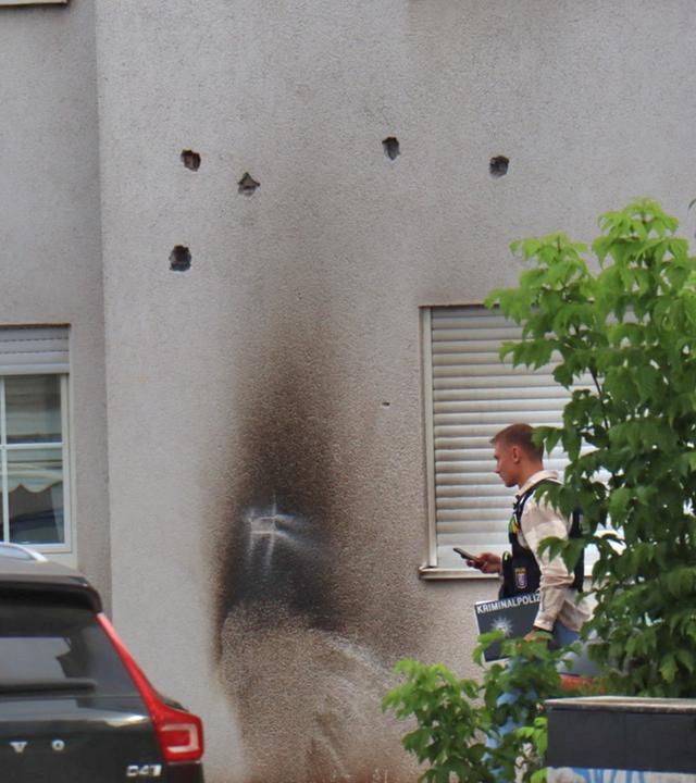 Auf dem Bild zu sehen: Die Fassade eines Wohnhauses in Lampertheim weist mehrere Einschusslöcher auf. In der Mitte der Hauswand sind deutliche Rußspuren zu sehen, die auf einen Brandkörper hindeuten.