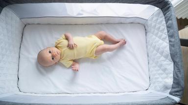Ein Baby liegt auf dem Rücken in einem Babybett.