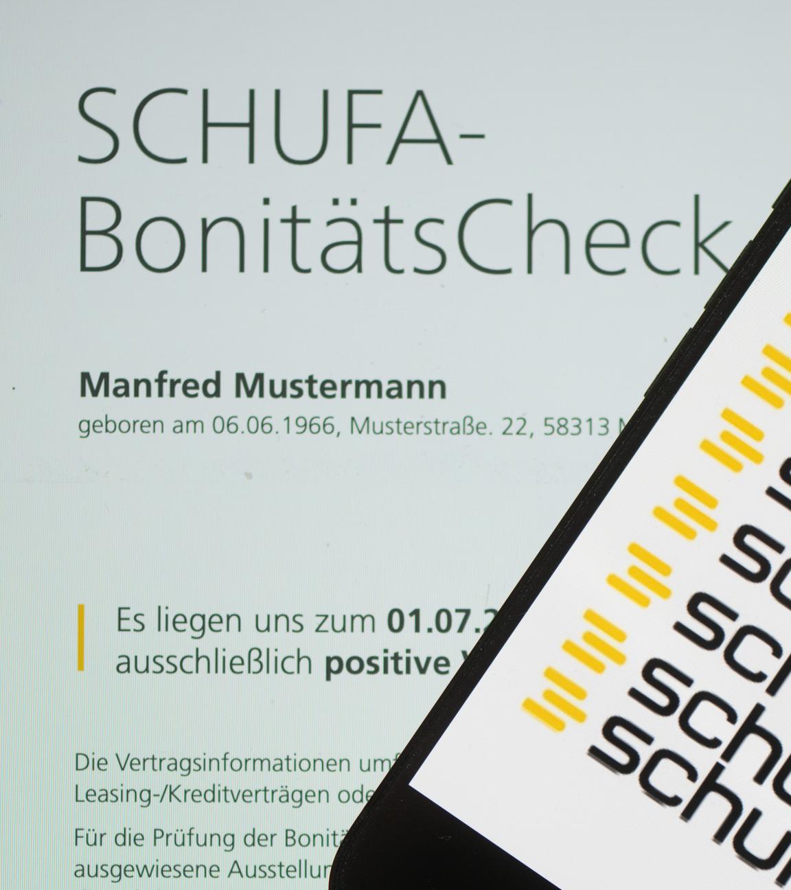 Ein Smartphone mit dem Logo der Wirtschaftsauskunftei Schufa liegt auf einem Display mit einem Musterdokument eines Schufa-Bonitätszertifikat