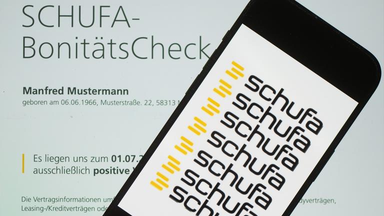 Ein Smartphone mit dem Logo der Wirtschaftsauskunftei Schufa liegt auf einem Display mit einem Musterdokument eines Schufa-Bonitätszertifikat