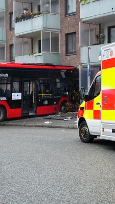 Ein Rettungswagen steht neben einem verunfallten Bus, der vor einer Hauswand steht.