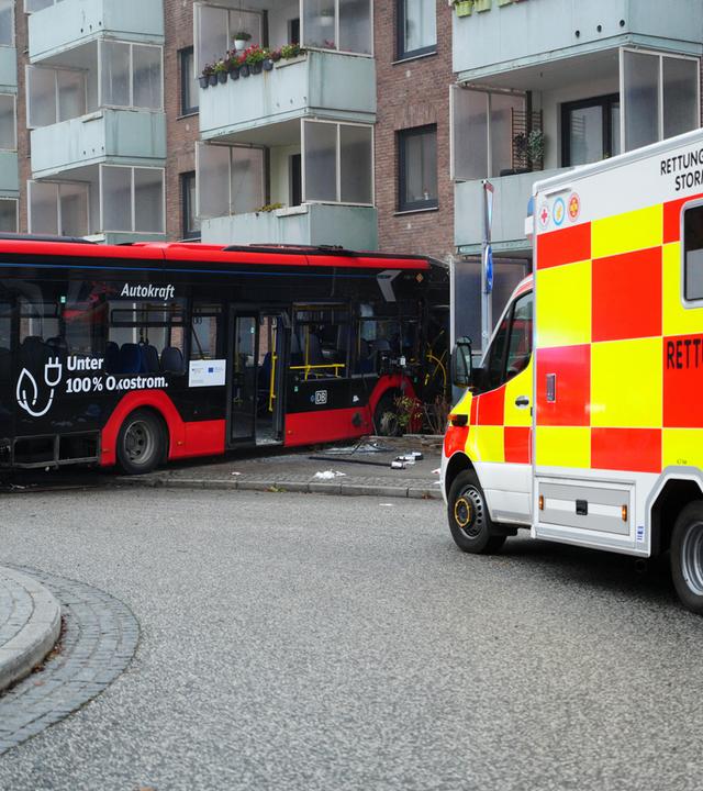 Ein Rettungswagen steht neben einem verunfallten Bus, der vor einer Hauswand steht.