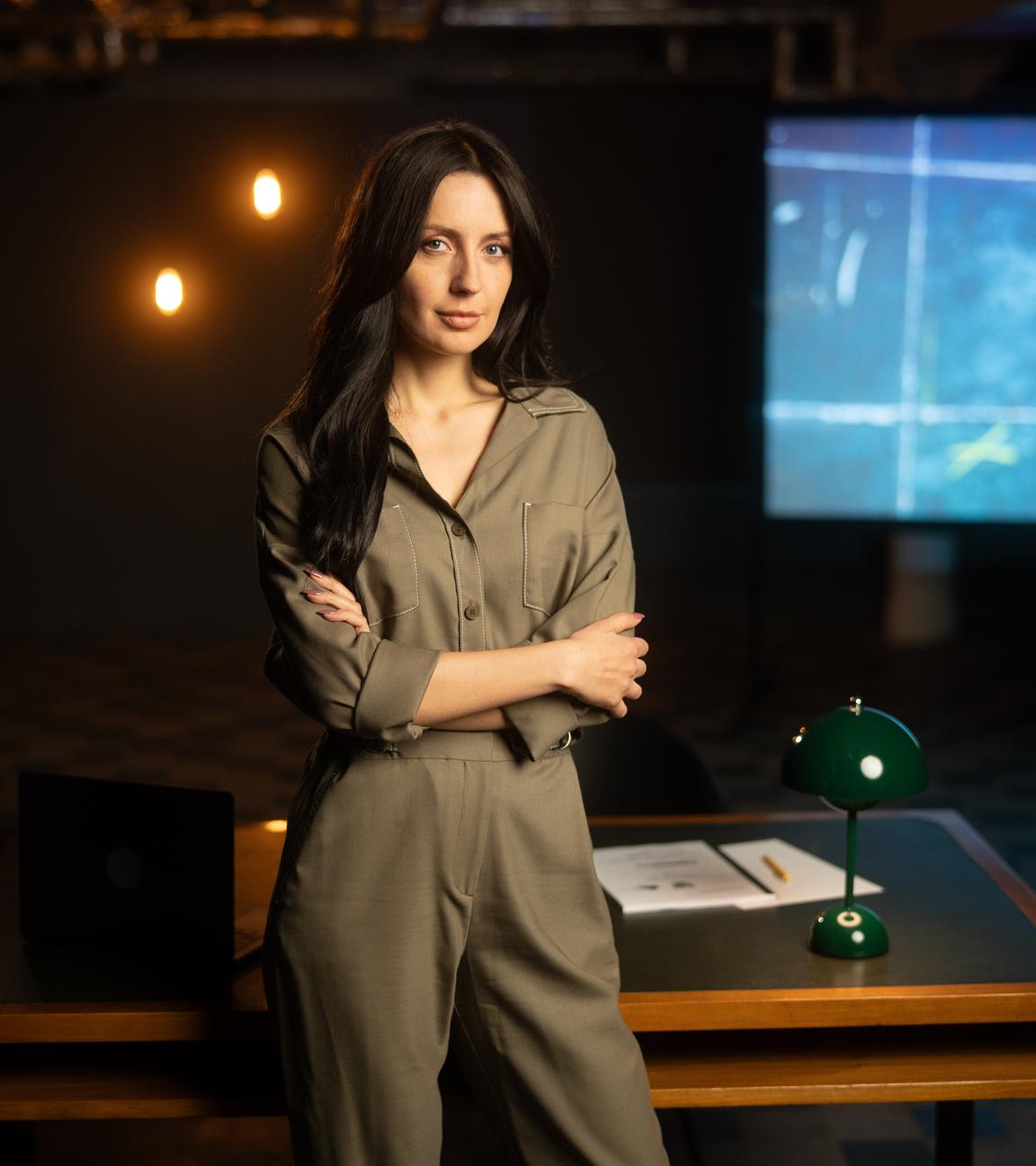 Paulina Krasa steht in einer Studiokulisse lächelnd mit verschränkten Armen vor einem Schreibtisch und blickt in die Kamera.