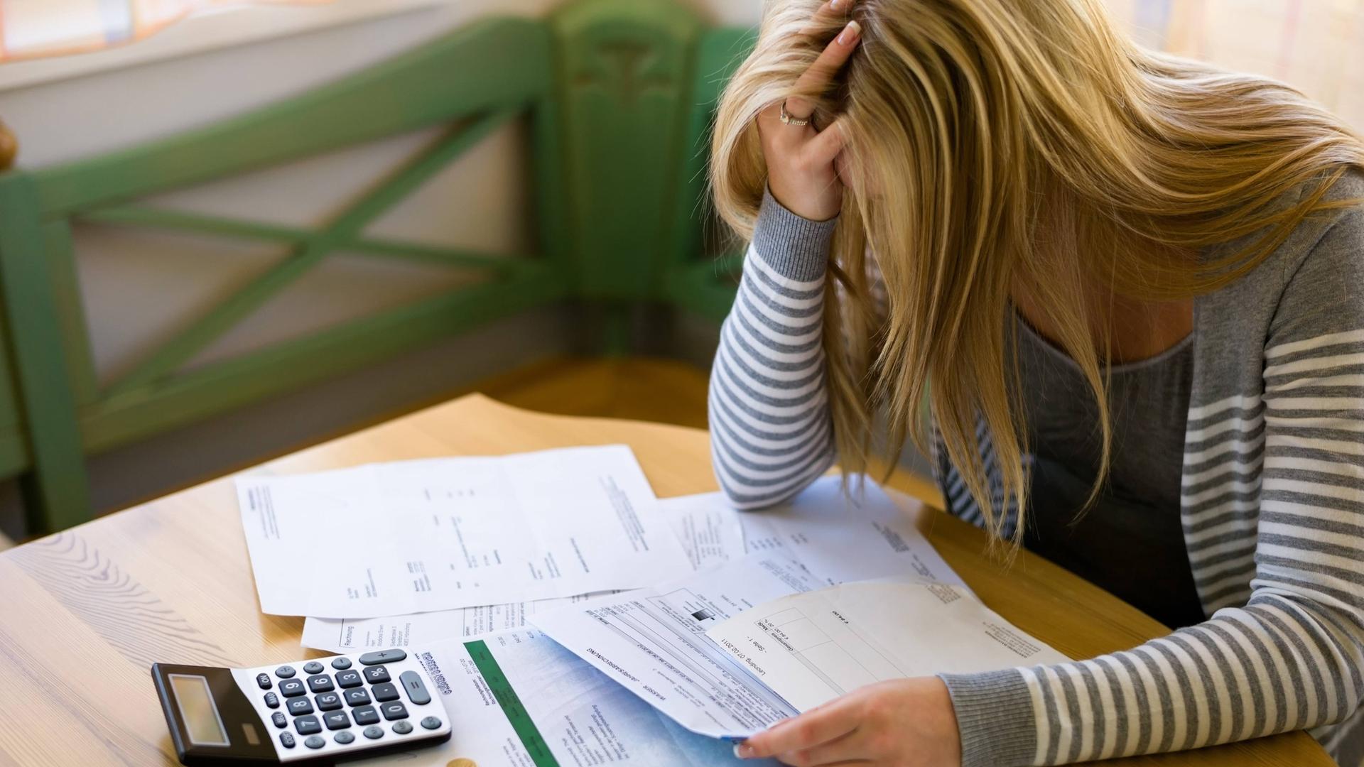 Symbolbild: Verzweifelte Frau sitzt vor Rechnungen