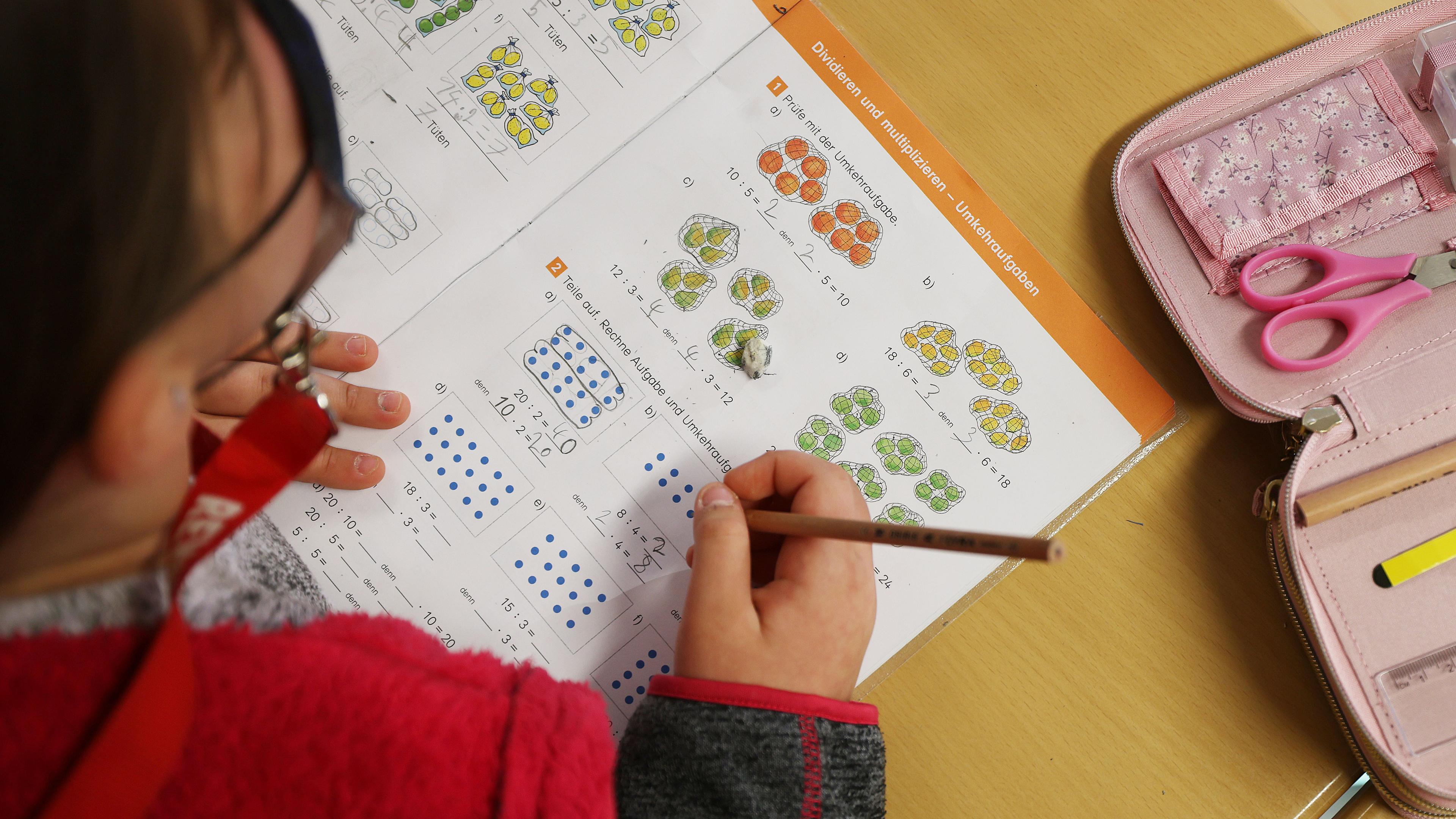 Eine Schülerin schreibt im Unterricht in ihr Schulbuch und löst eine Rechenaufgabe.
