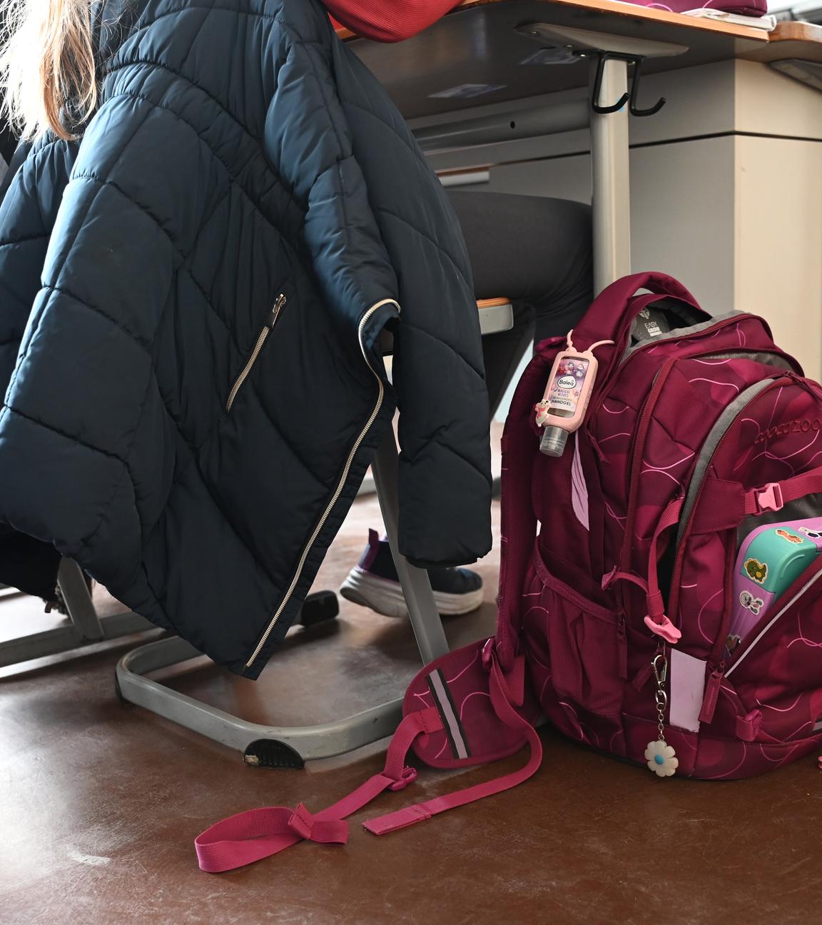 Eine Person sitzt an einem Tisch. Daneben steht ein voller Schulrucksack.