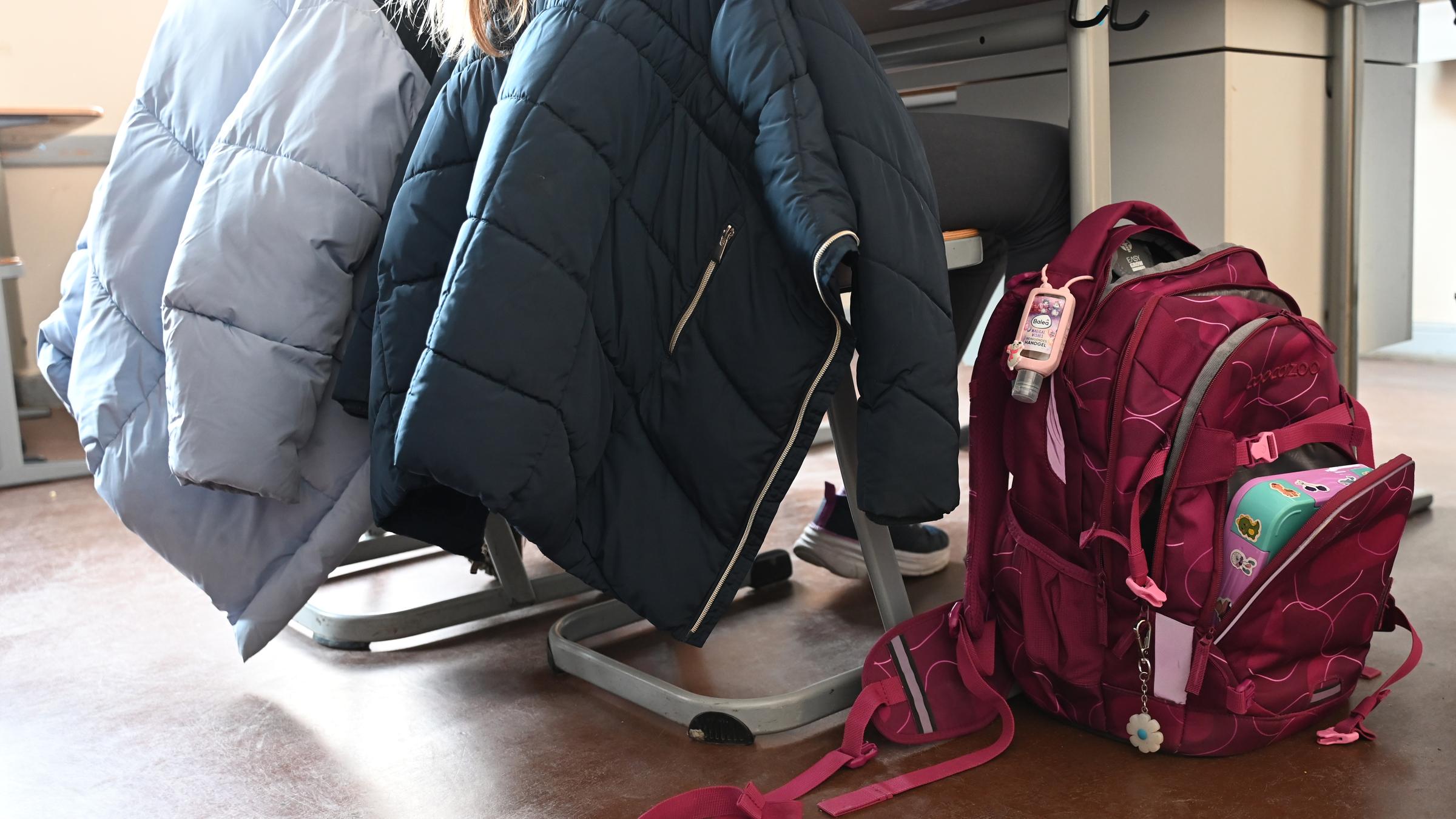 Eine Person sitzt an einem Tisch. Daneben steht ein voller Schulrucksack.