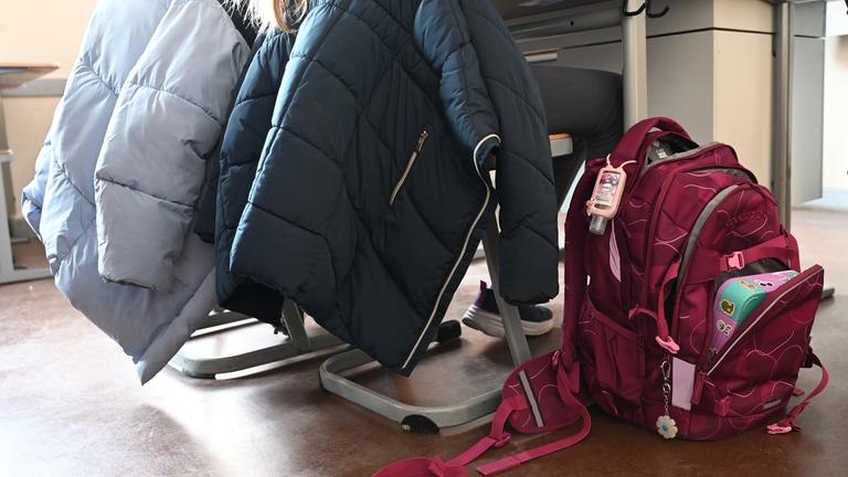 Eine Person sitzt an einem Tisch. Daneben steht ein voller Schulrucksack.