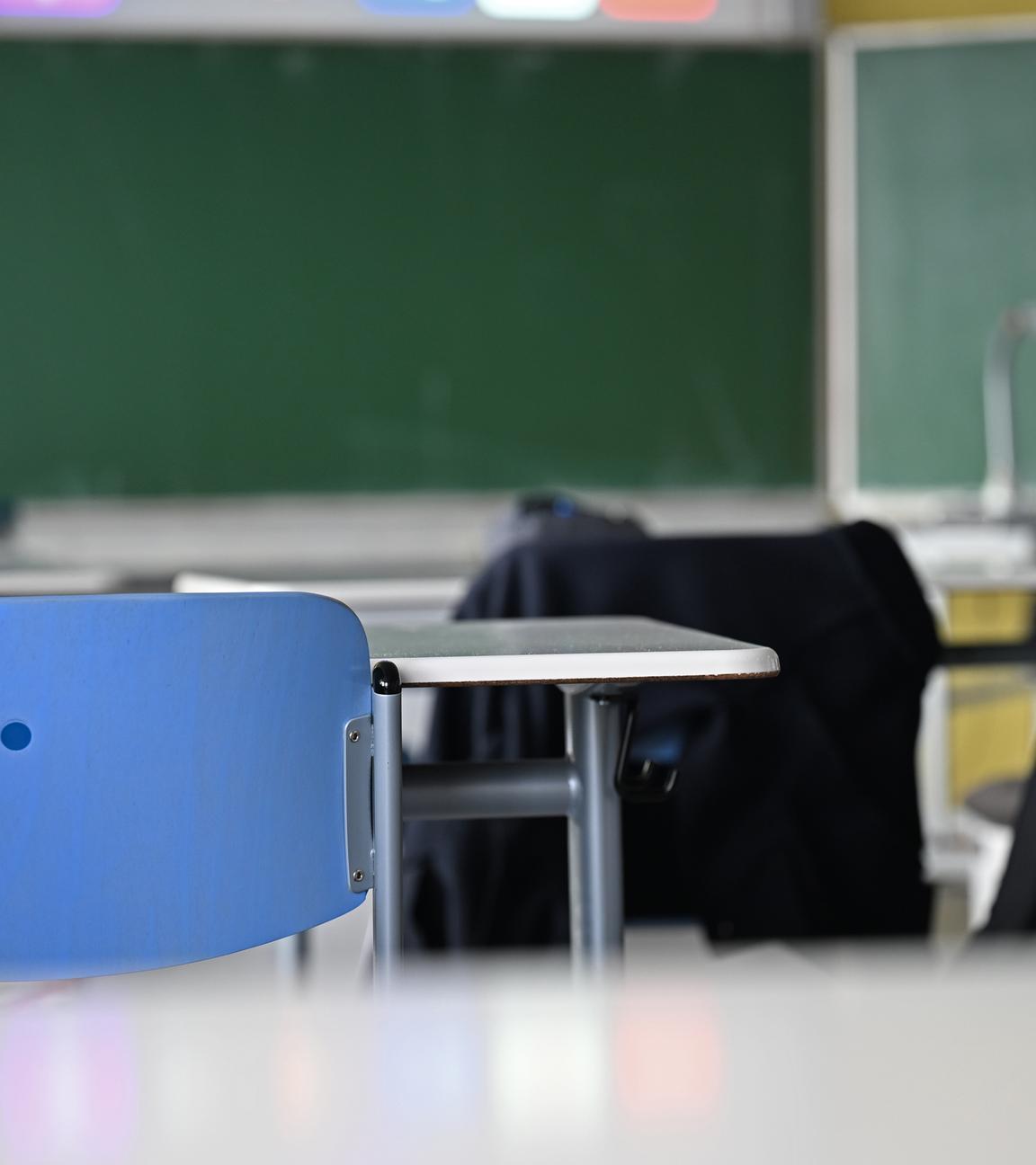 Leere Stühle und Tische stehen in einem Klassenraum vor einer Tafel.