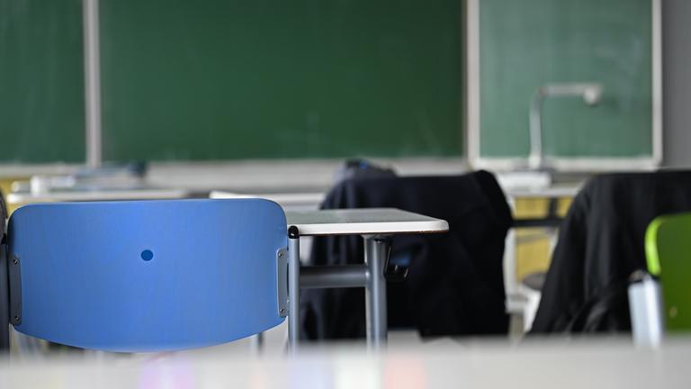 Leere Stühle und Tische stehen in einem Klassenraum vor einer Tafel.