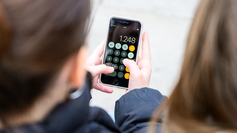 Kinder mit Smartphone in der Hand. Darauf ist die Taschenrechner-App geöffnet.