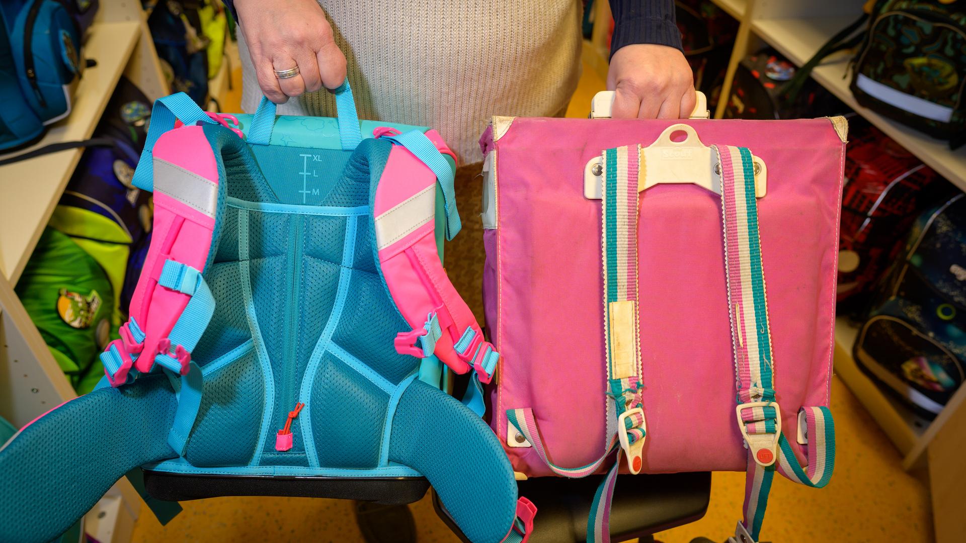 Eine Verkäuferin hält zwei Schulranzen zum Vergleich nebeneinander.