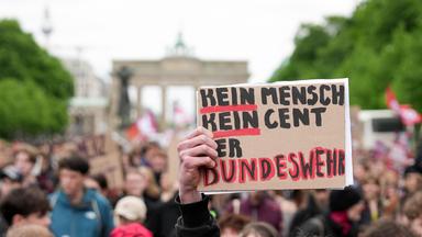 Eine Hand hält ein Schild mit der Aufschrift "Kein Mensch, kein Cent der Bundeswehr" während zahlreiche Demonstranten, am 08.05.2026, in Berlin gegen die Wehrpflicht protestieren.
