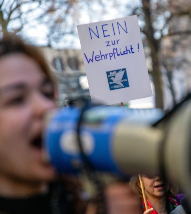 Eine junge Frau spricht in ein Megafon, während hinter ihr ein Plakat mit der Aufschrift "Nein zur Wehrpflicht!" in die Höhe gehalten wird. (Archivbild)
