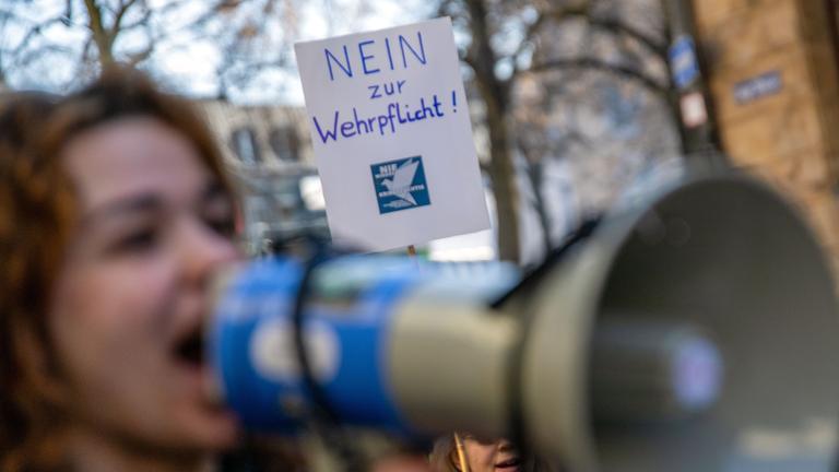 Eine junge Frau spricht in ein Megafon, während hinter ihr ein Plakat mit der Aufschrift "Nein zur Wehrpflicht!" in die Höhe gehalten wird. (Archivbild)