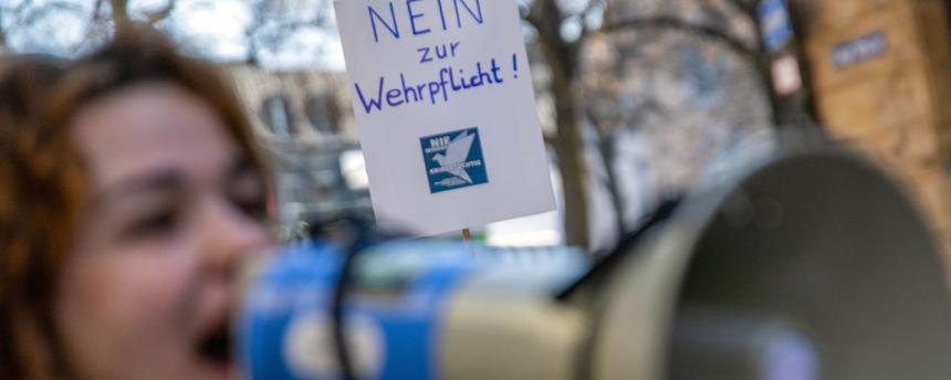 Eine junge Frau spricht in ein Megafon, während hinter ihr ein Plakat mit der Aufschrift "Nein zur Wehrpflicht!" in die Höhe gehalten wird. (Archivbild)