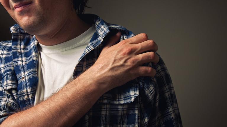 Ein Mann hält sich die Schulter mit einem schmerzverzerrtem Gesicht.