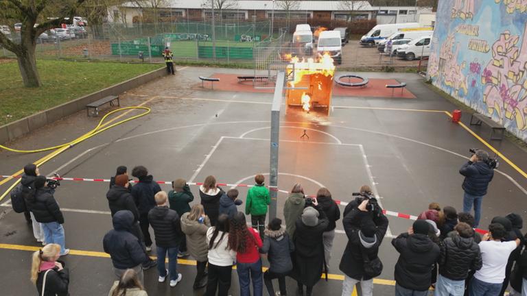 Eine Schulklasse beobachtet, wie die Feuerwehr Feuer simuliert