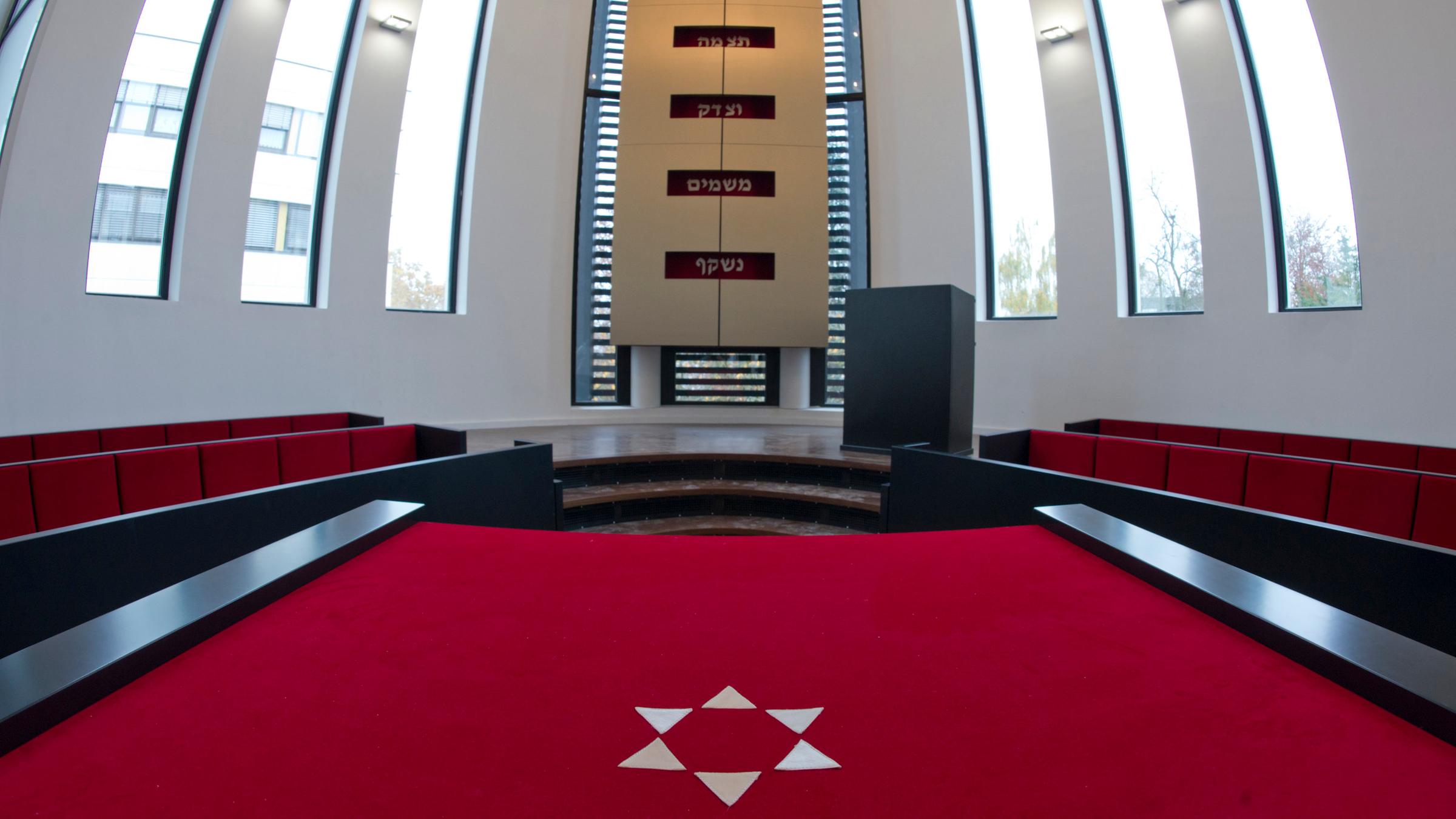 Ein Teil der Synagoge in Speyer ist abgebildet mit rotem Teppich und großen Fenstern.