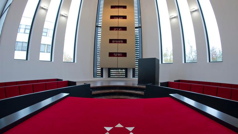 Ein Teil der Synagoge in Speyer ist abgebildet mit rotem Teppich und großen Fenstern.