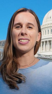 US-Korrespondentin Katharina Schuster steht in einem blauen Oberteil mit kurzen Ärmeln auf dem Rasen vor dem US-Kongressgebäude in Washington DC und spricht in die Kamera. Ihre langen braunen Haare fallen ihr über die rechte Schulter nach vorne. Sie trägt eine dunkle Hose.
