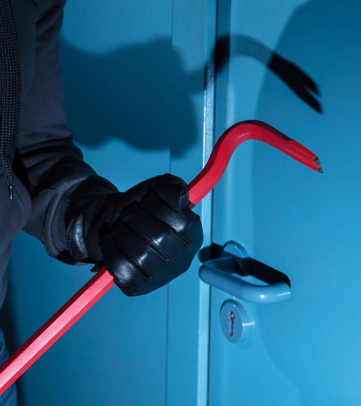 Einbrecher mit Werkzeug vor blauer Wohnungstür