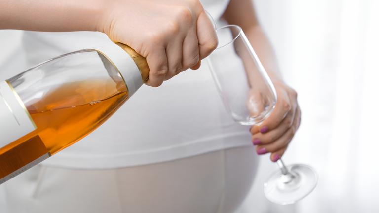 Schwangere Frau gießt sich ein alkoholisches Getränk in ein Glas.
