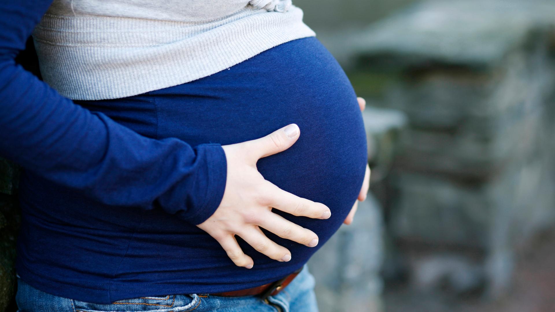 Schwangere Frau hält ihren Bauch mit beiden Händen