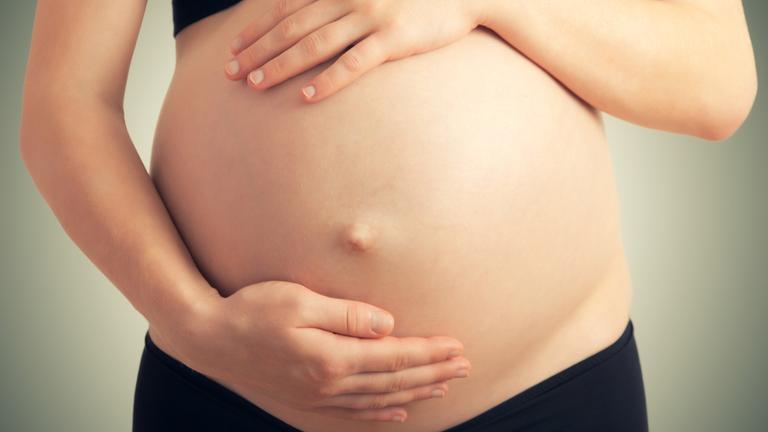 Eine schwangere Frau hält mit beiden Händen ihren Bauch.