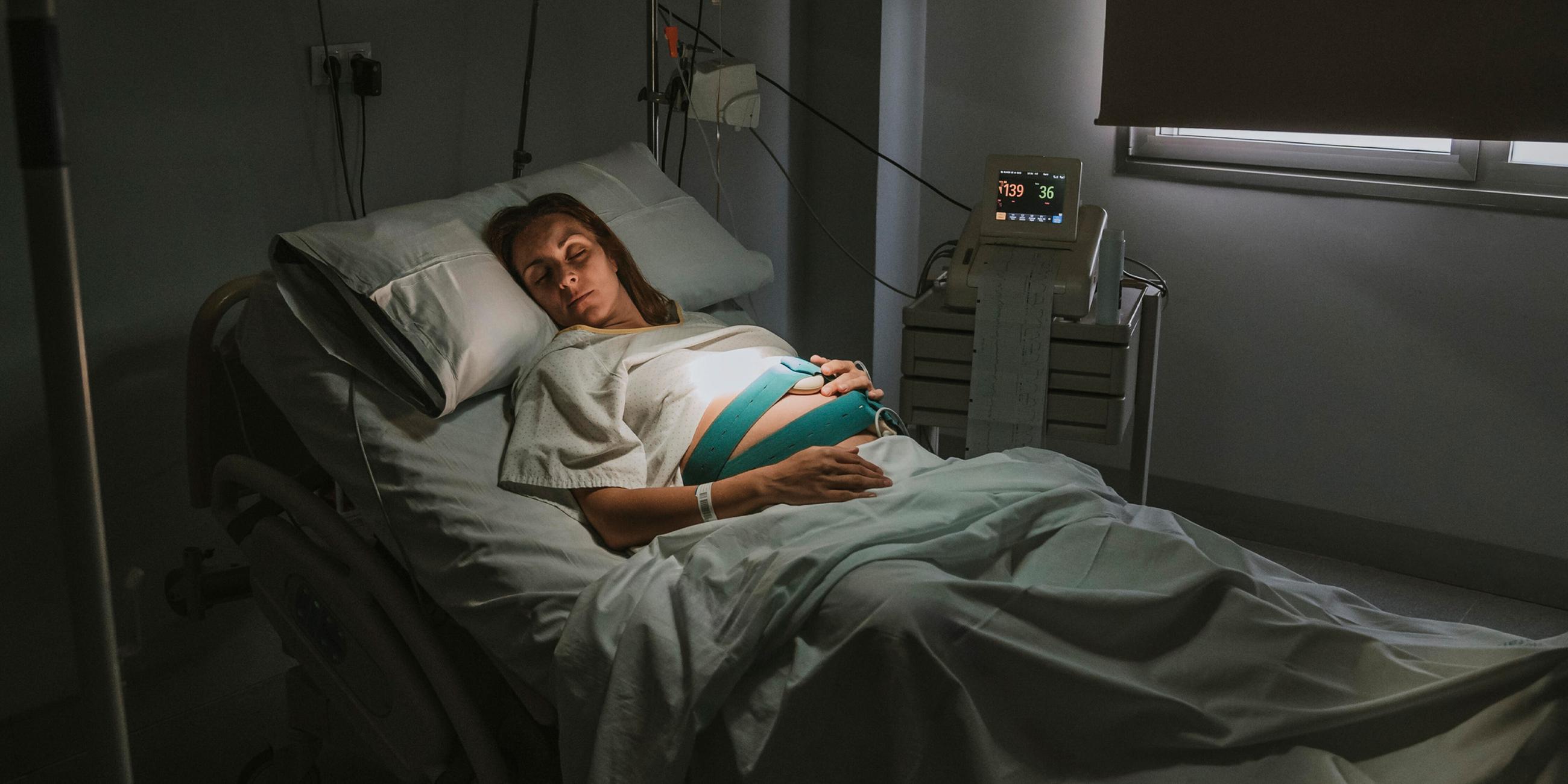 Schwangere Frau schläft auf dem Bett in der Nähe von Geräten im Kreißsaal im Krankenhaus. (Symbolbild)