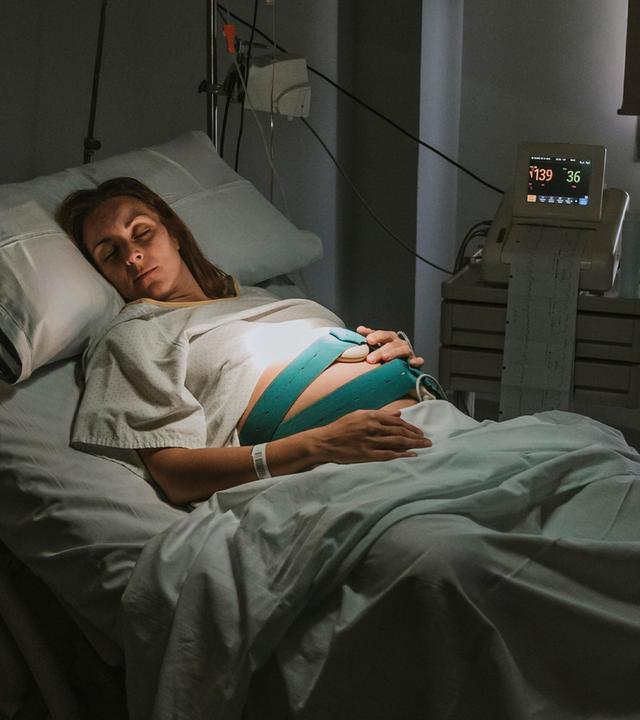 Schwangere Frau schläft auf dem Bett in der Nähe von Geräten im Kreißsaal im Krankenhaus. (Symbolbild)