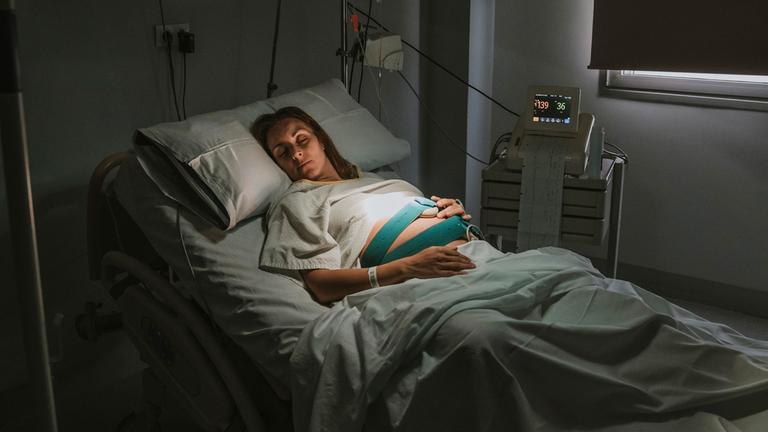 Schwangere Frau schläft auf dem Bett in der Nähe von Geräten im Kreißsaal im Krankenhaus. (Symbolbild)