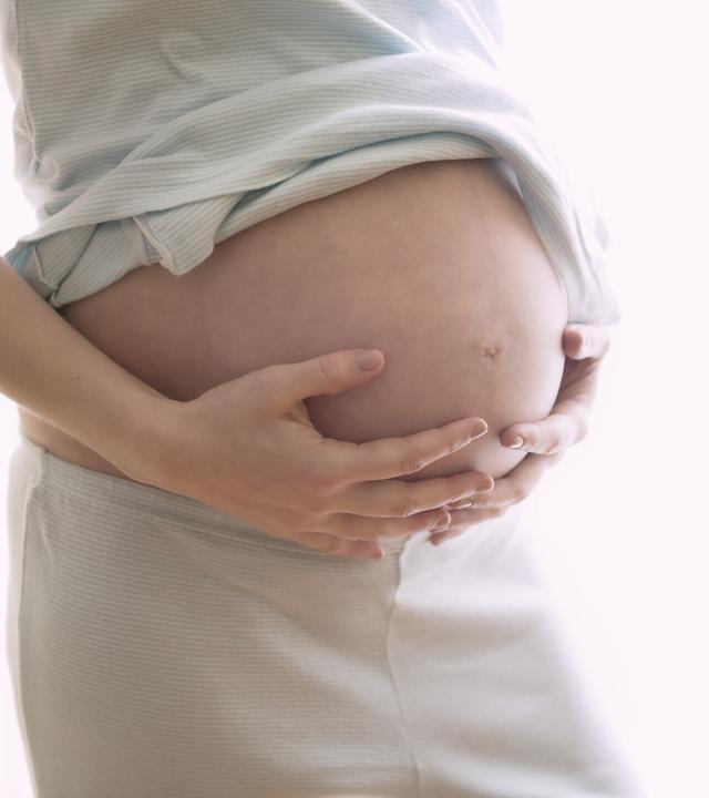 Schwangere Frau hält sich den Bauch.