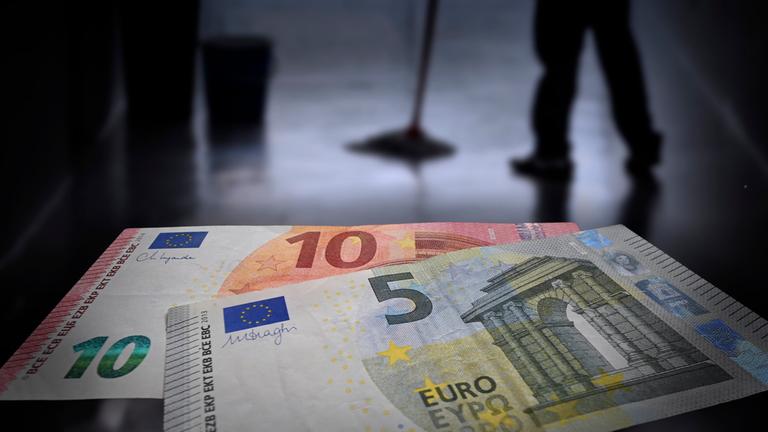 Die Silouhette einer Reinigungskraft, davor zwei Geldscheine, die in die Kamera gehalten werden.