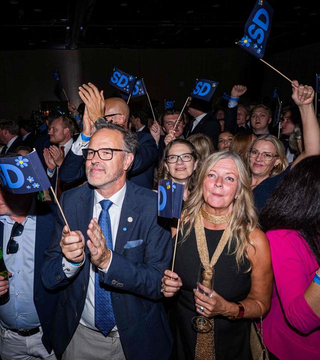 Politiker der schwedischen Partei Schwedendemokraten wedeln mit Wimpeln ihrer Partei oder klatschen in die Hände.