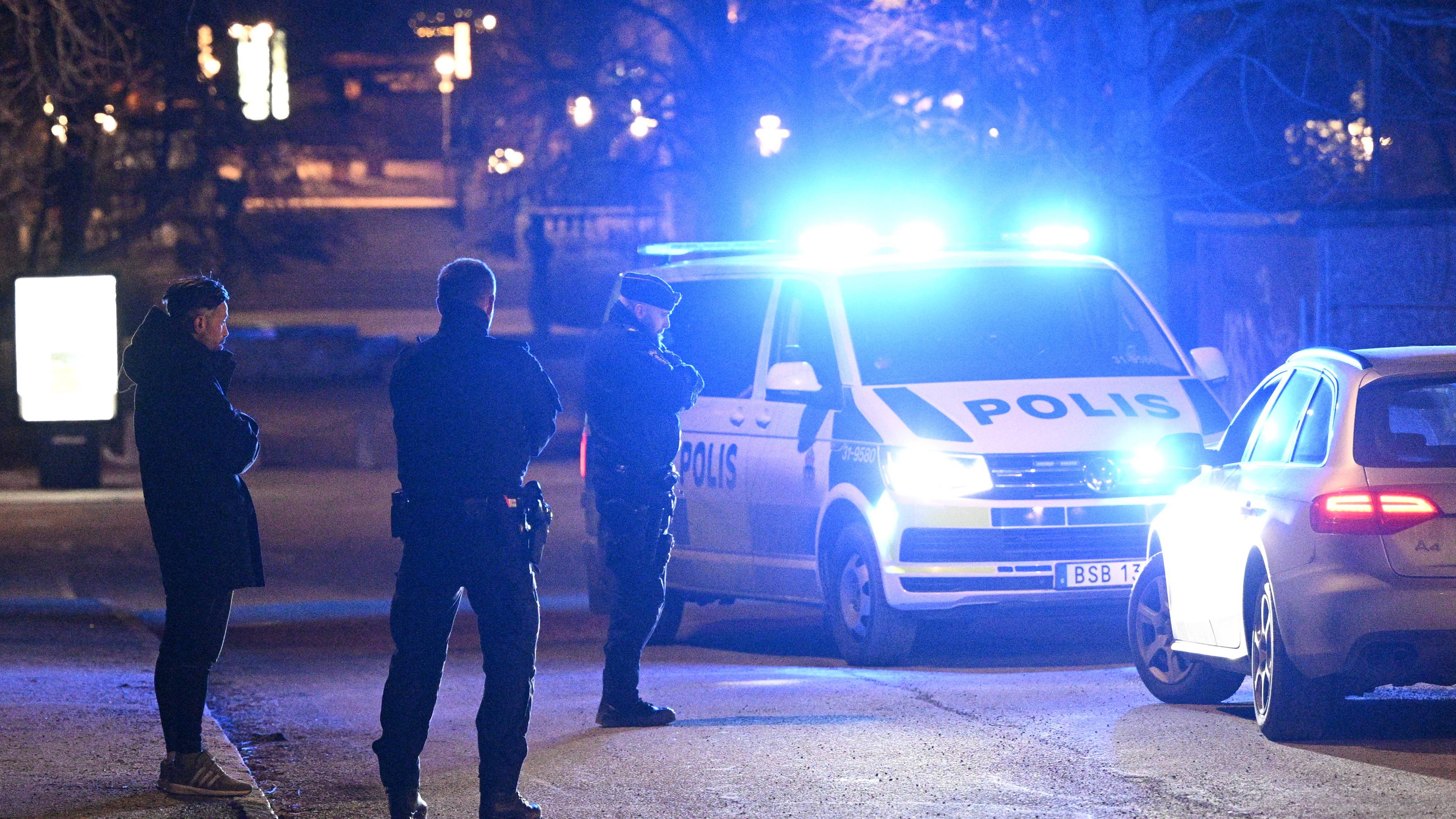 Neben einem schwedischen Polizeiauto stehen Polizisten und eine weitere Person.