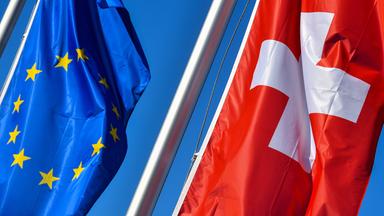 Die Nationalflagge der Schweiz weht neben der Flagge der EU vor blauem Himmel.