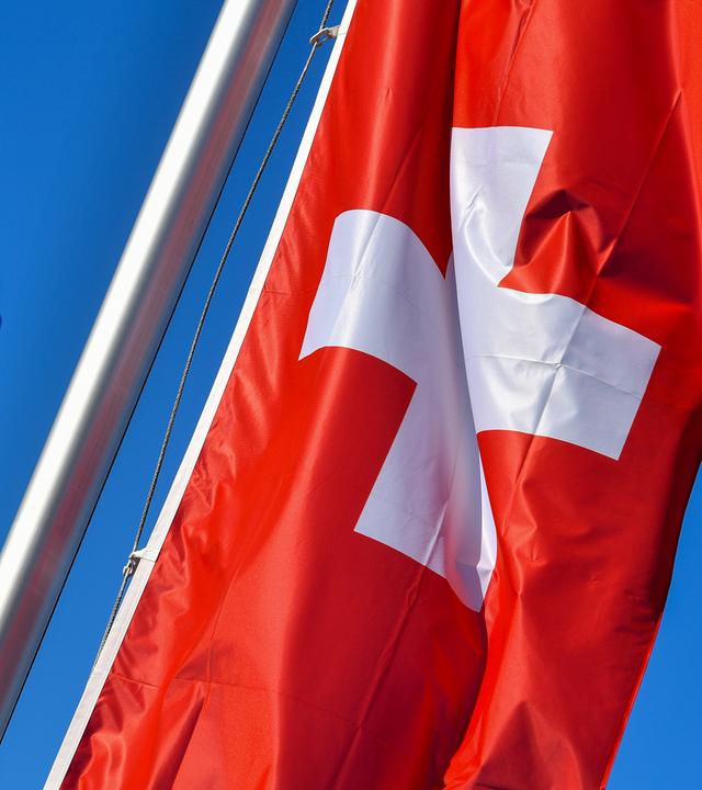 Die Nationalflagge der Schweiz weht neben der Flagge der EU vor blauem Himmel.