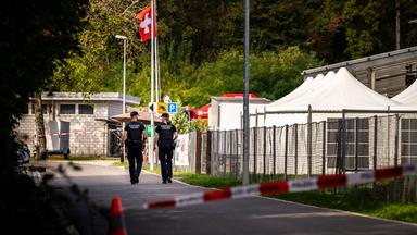 Auf dem Bild sind 2 Polizist*innen zu sehen die hinter Absperrband laufen.