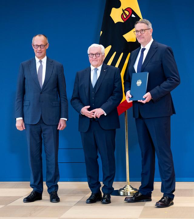 Friedrich Merz, Frank-Walter Steinmeier und Alexander Schweitzer bei der Ansprache und Aushändigung der Ernennungsurkunde an Alexander Schweitzer zum Bundesminister für Arbeit und Soziales. Sie stehen alle nebeneinander.