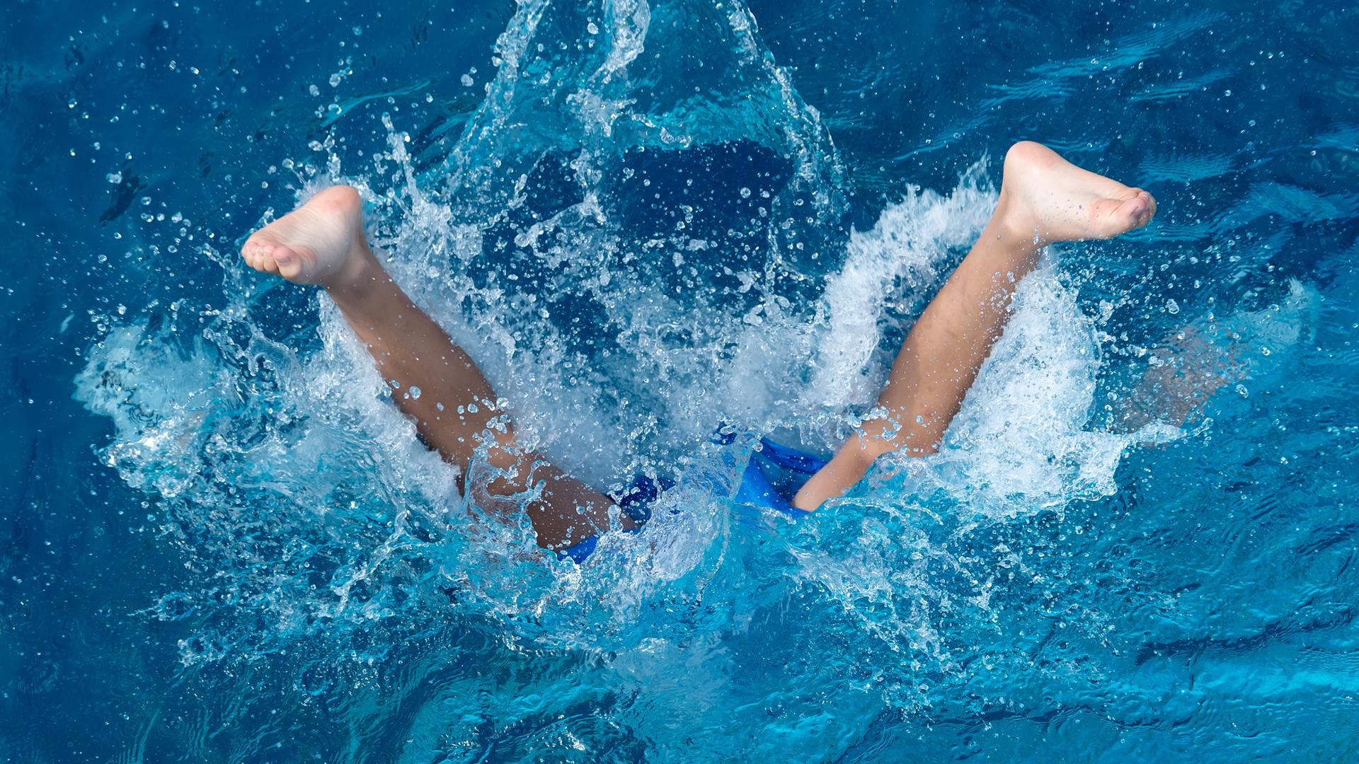 Ein Kind taucht in ein Schwimmbecken ein.