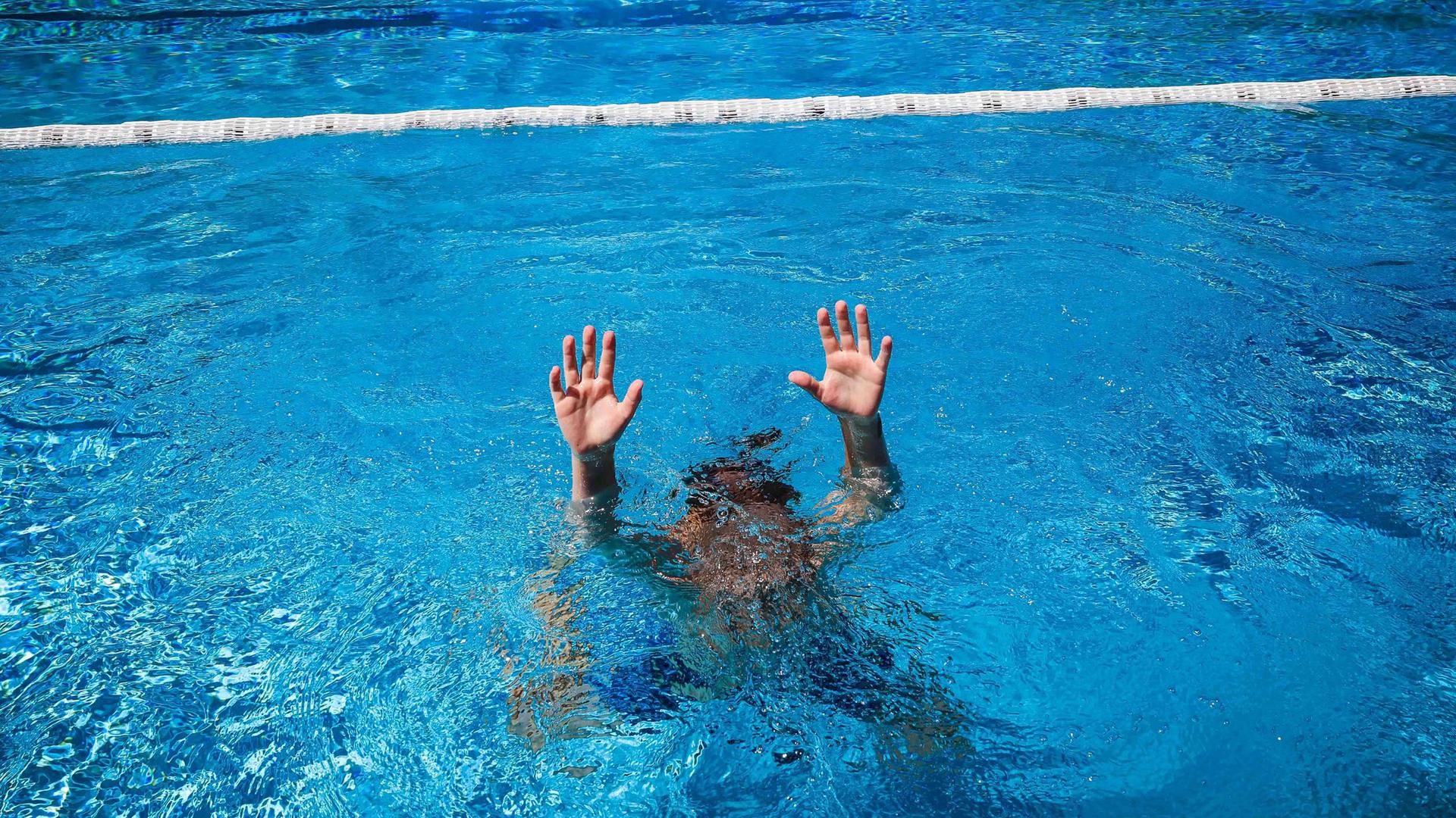 (Symbolbild) Ein Kind versucht im Schwimmbecken auf sich aufmerksam zu machen.
