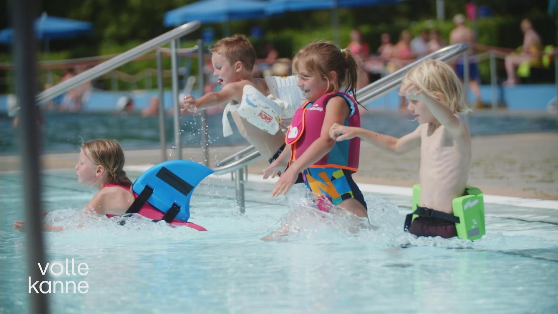 Vier Kinder gehen mit verschiedenen Schwimmhilfen ins Schwimmbecken.