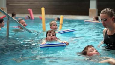 Kinder im Wasser mit Schwimmnudel und -brett beim Schwimmunterricht